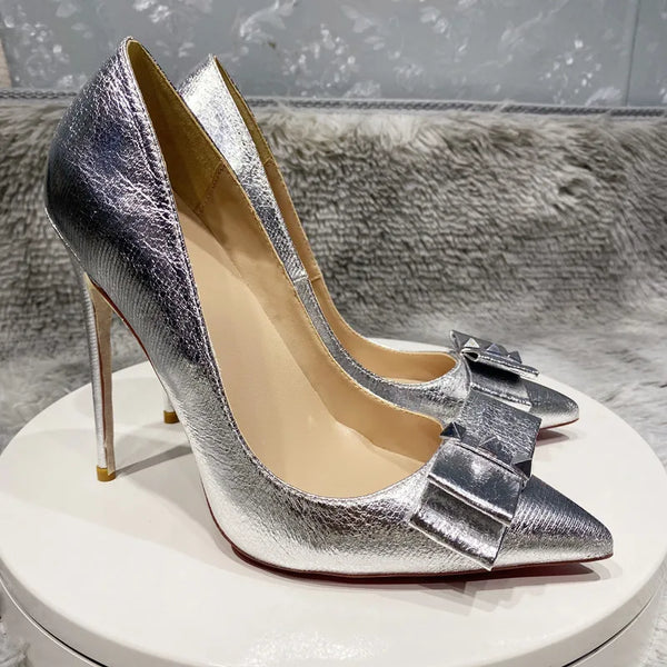 Tacones altos plateados para mujer con lazo y punta de metal.