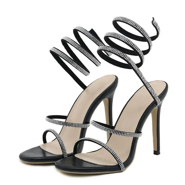 Tacones altos negros de moda con punta abierta y tiras en el tobillo con cristales y pedrería